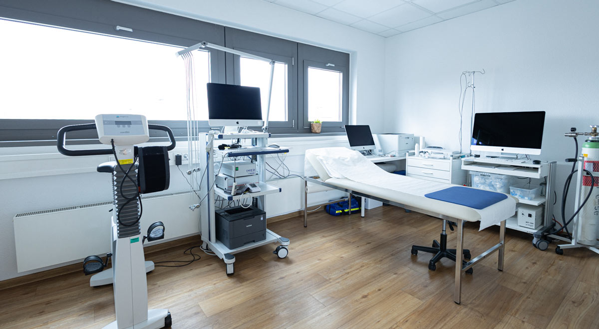 Bild zeigt einen Untersuchungsraum mit Liege, Sportfahrrad und diversen medizinischen Geräten